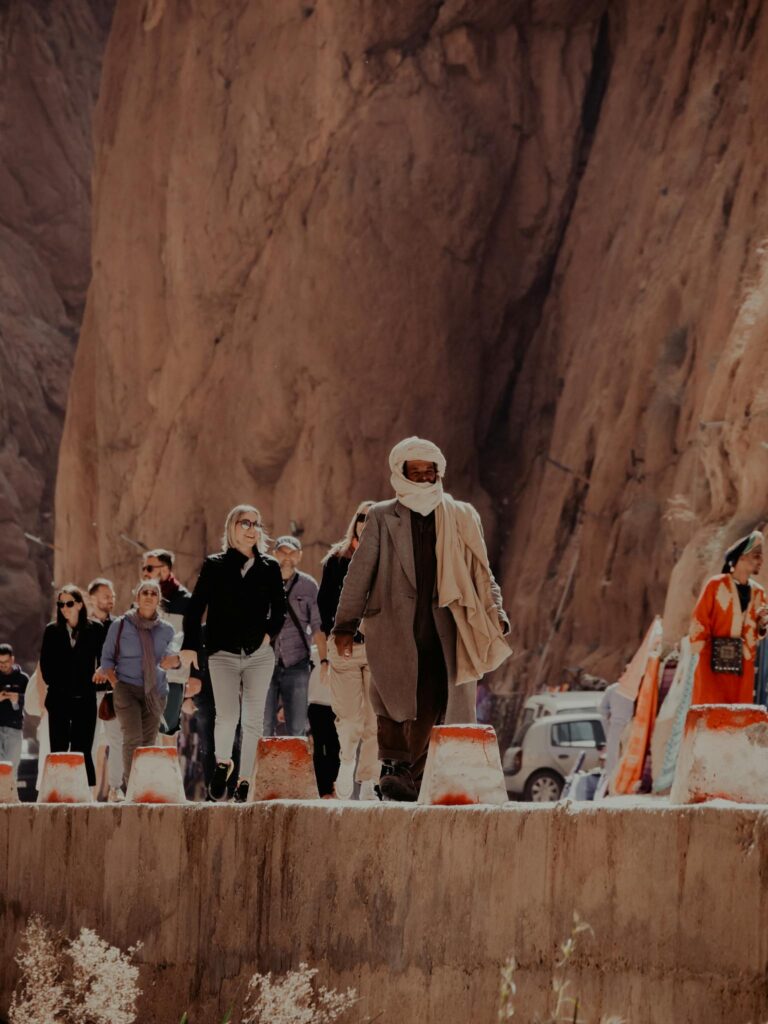 Group of tourists with a desert guide walking through a canyon in Marrakesh, Morocco under bright sunlight.