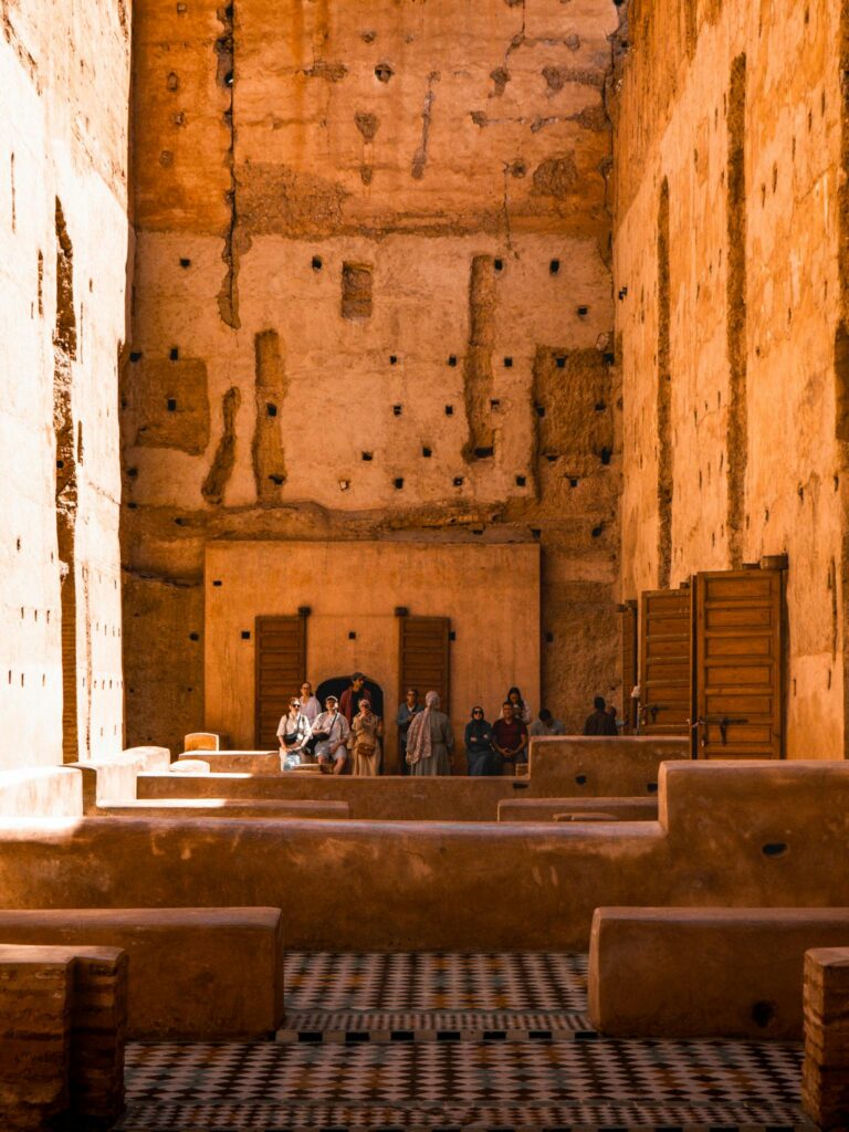 Visitors exploring the intricate architecture of a historic Marrakesh palace under warm sunlight.